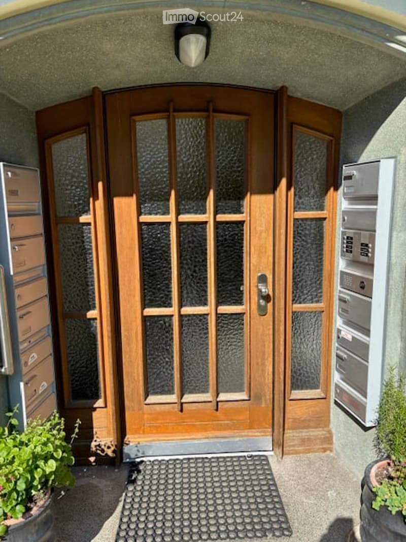 Entrance area with a large wooden double door featuring glass panels, a welcome mat, and mailboxes on either side.