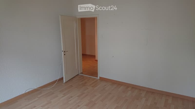 Empty room with light wooden flooring and white walls, featuring an open doorway leading to another room.