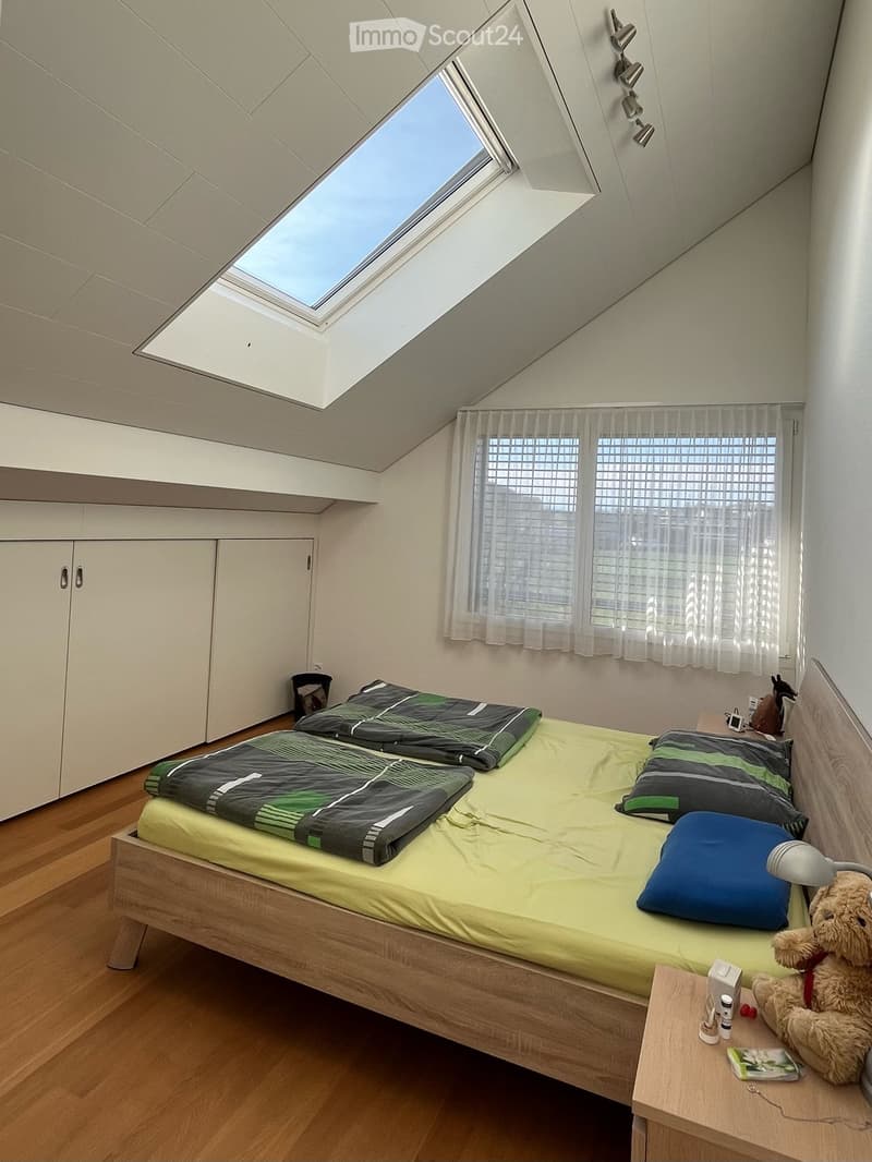 Modern bedroom with a single bed, green and black bedding, pillows, a nightstand with a lamp, and a teddy bear. Features a skylight window and built-in wardrobes.