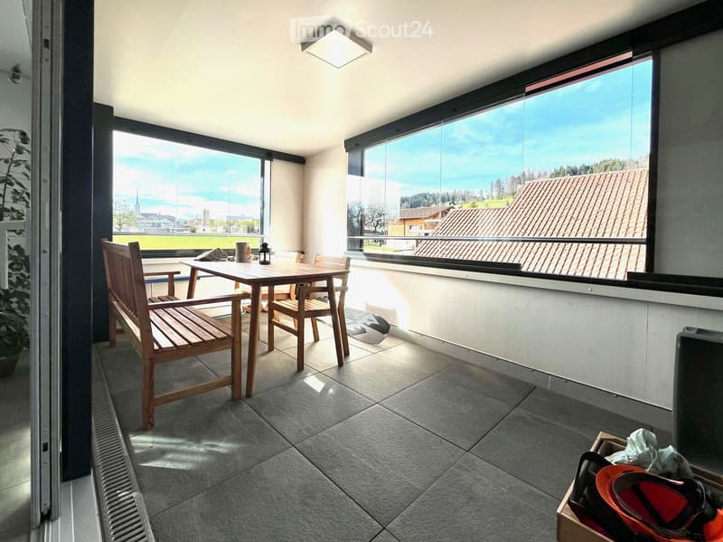 Balcony with large windows offering a scenic view, furnished with a wooden table, chairs, and a lantern.
