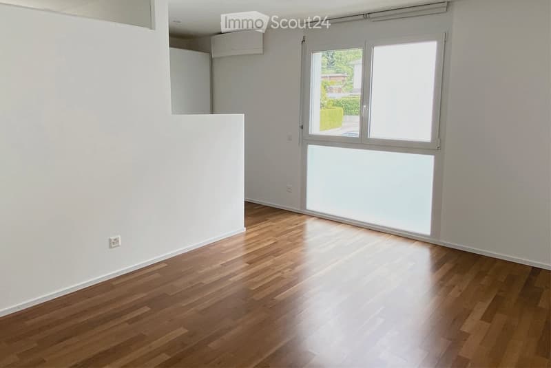 Empty room with wooden flooring and white walls, featuring a large window with blinds and an air conditioning unit on the wall.