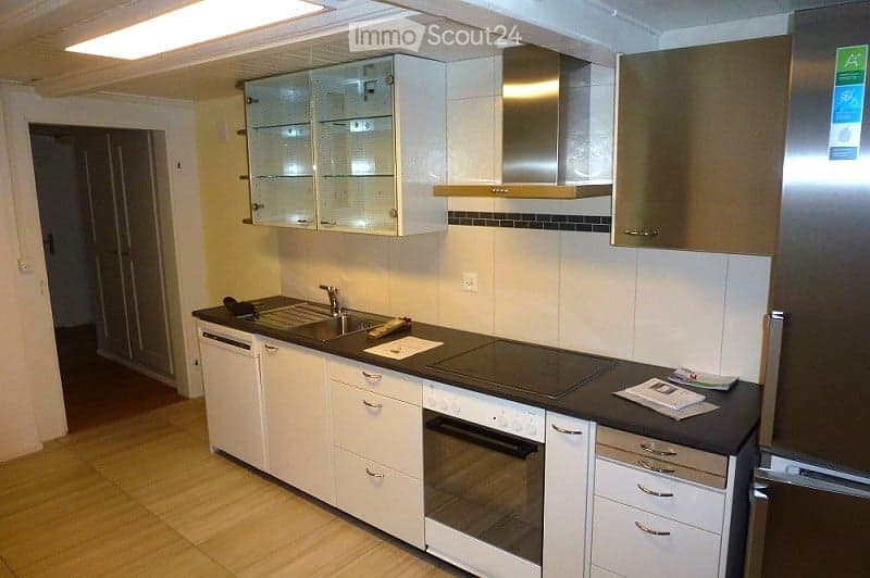 Modern kitchen with white cabinets, stainless steel appliances, and a black countertop. Features include a sink, faucet, oven, refrigerator, and range hood.