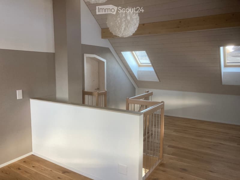 Bright hallway with wooden flooring, white walls, and a staircase leading upwards. Features a skylight window and a hanging decorative light fixture.