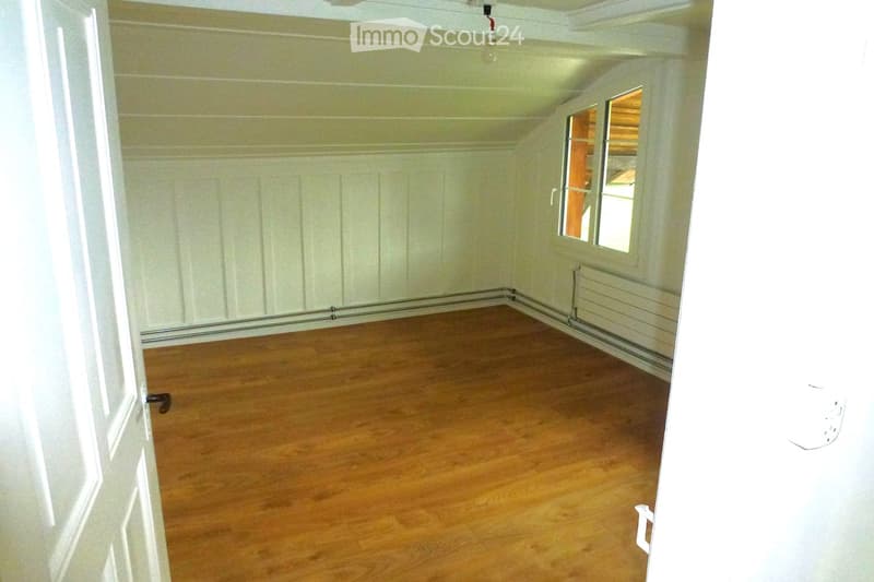 Empty room with wooden flooring, white walls, and a window with a view of another room.