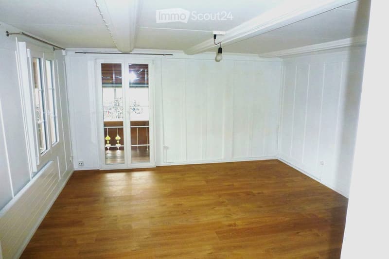 Empty room with wooden flooring, white walls, and large windows. The space features a sliding glass door leading to a balcony area.