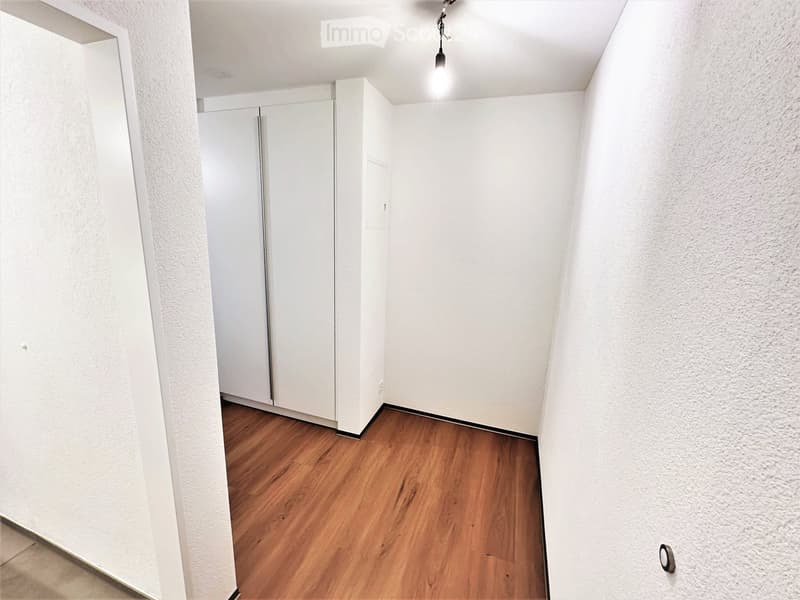 Empty hallway with wooden flooring, white walls, and a closed white door at the end.