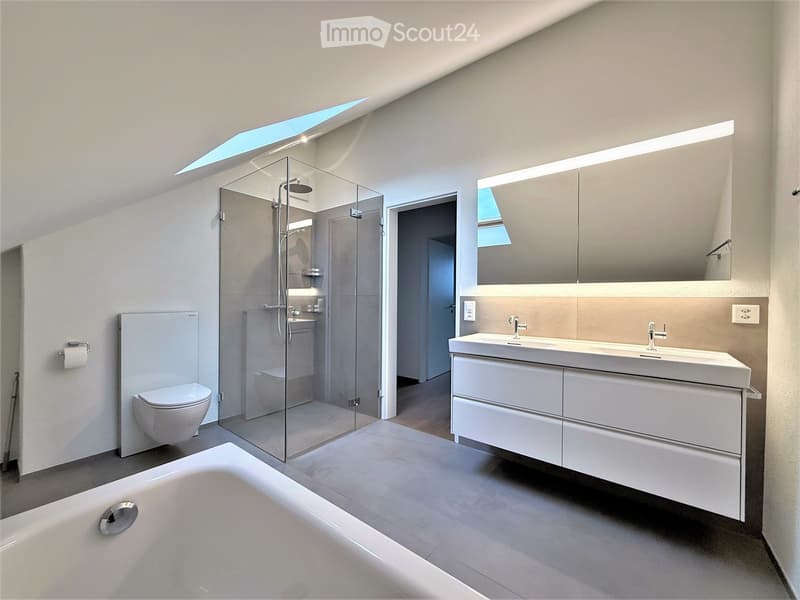 Modern bathroom with a bathtub, toilet, sink, mirror, and glass-enclosed shower. Features sleek white fixtures and a skylight window.