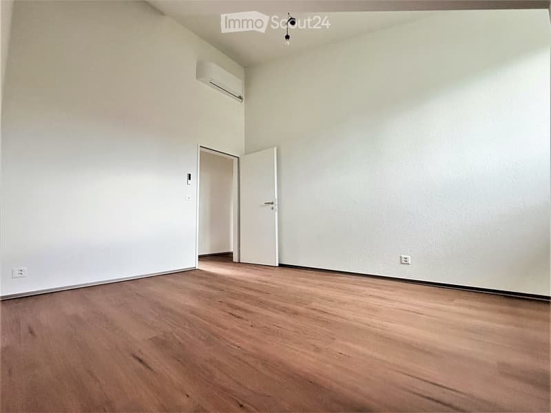 Empty room with wooden flooring, white walls, and a single open door leading to another space.