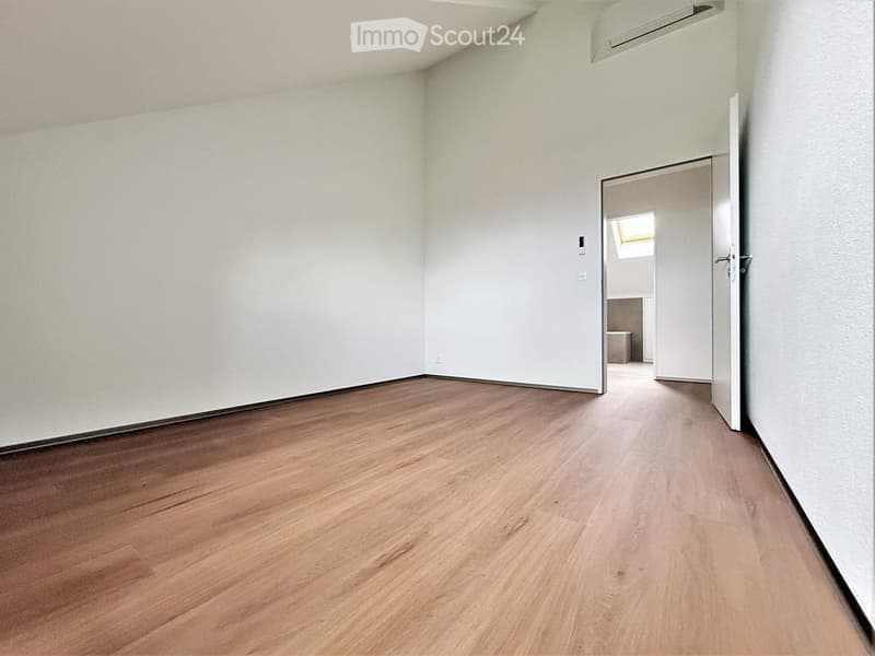 Empty room with light wooden flooring and white walls, featuring a partially open door leading to another space.
