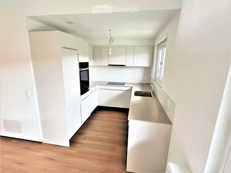 Modern, minimalist kitchen with white cabinets, a central island, and a wooden floor.