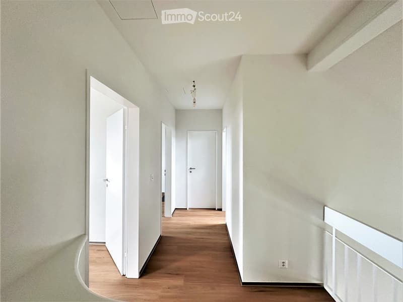 Empty hallway with light-colored walls, wooden flooring, and several white doors leading to rooms.