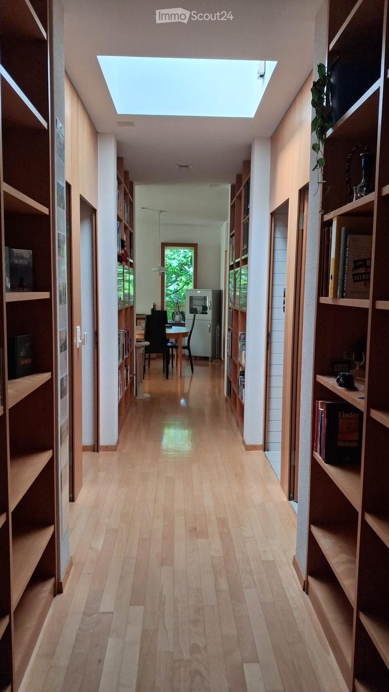 Bright hallway with wooden flooring, built-in bookshelves on both sides, and a skylight at the top. A small dining area is visible at the end of the hallway.