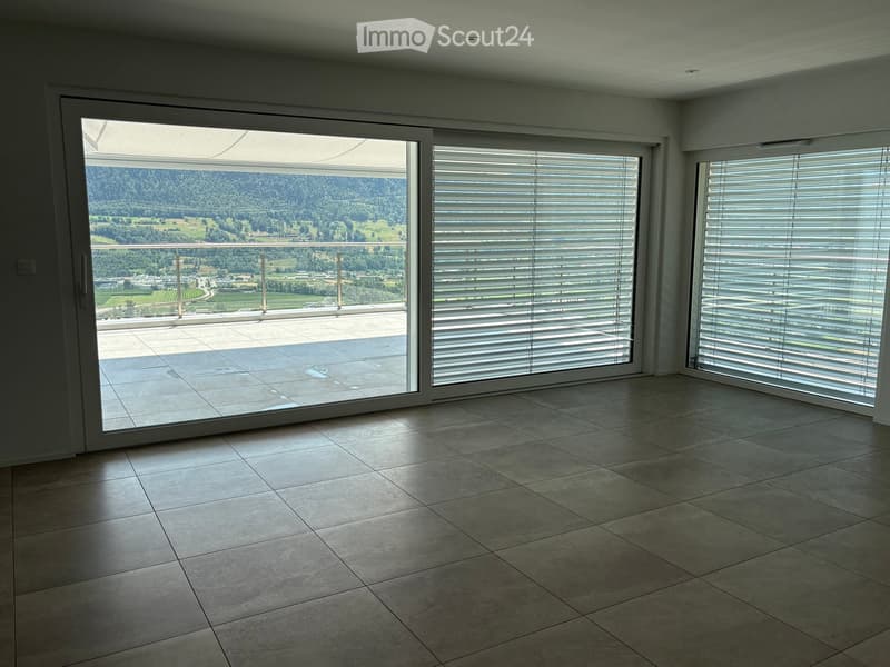 Empty room with large sliding glass doors leading to a balcony with a scenic mountain view. The room features tiled flooring and white walls.