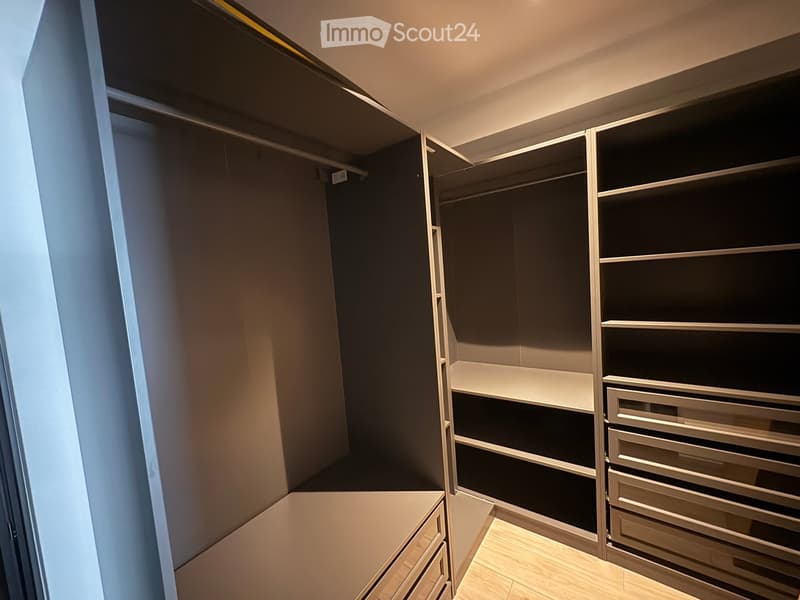 Empty walk-in closet with built-in shelves and drawers, light wood flooring, and neutral-colored walls.