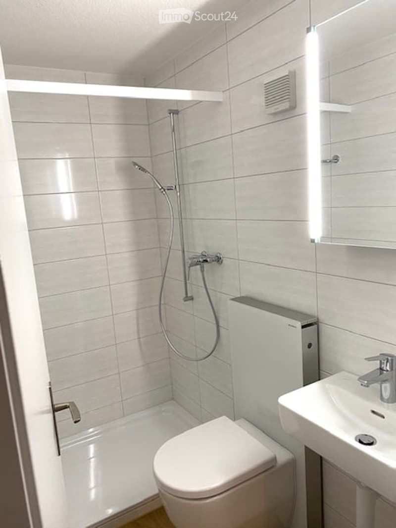 Modern bathroom with white tiles, a toilet, a sink, a shower, and a mirror.