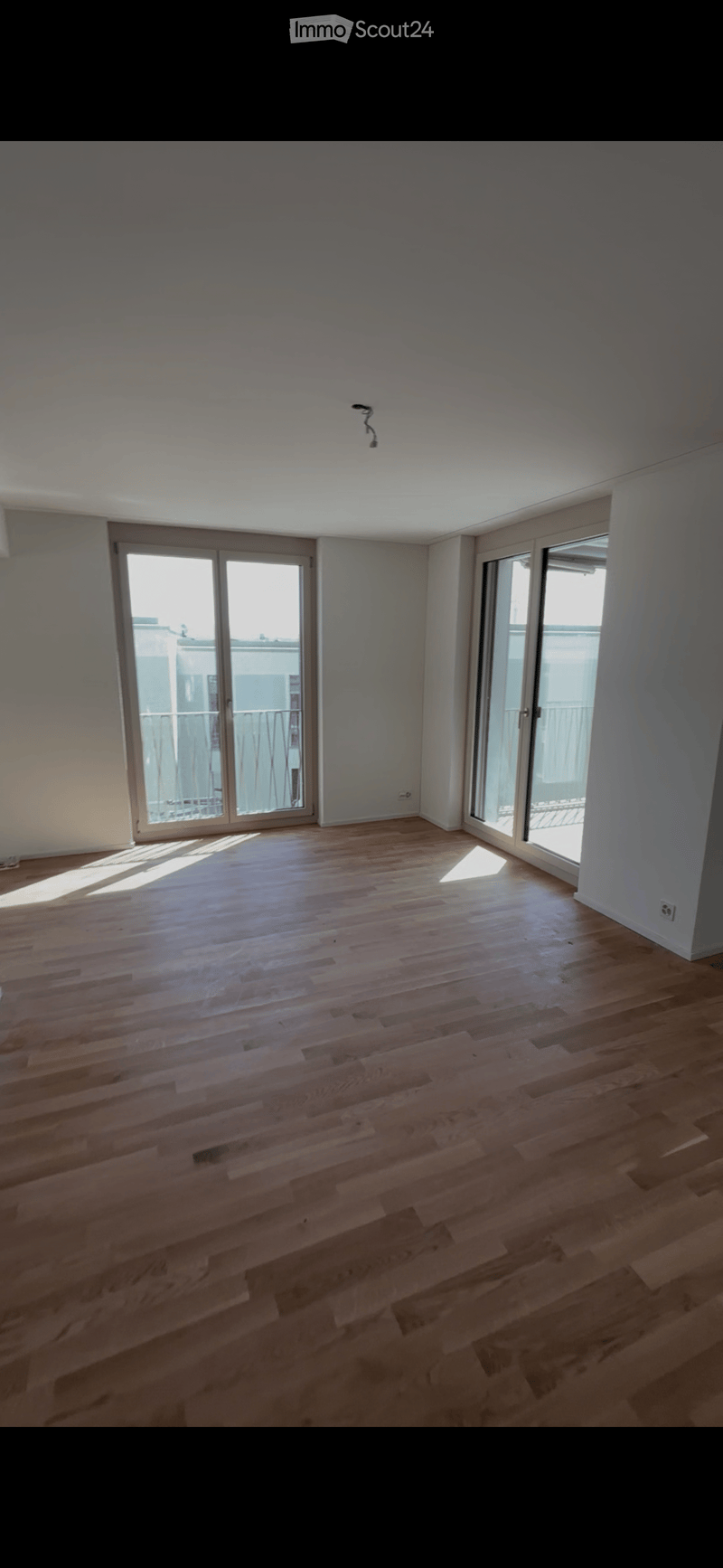 Empty room with wooden flooring, large windows, and sliding glass doors leading to a balcony.