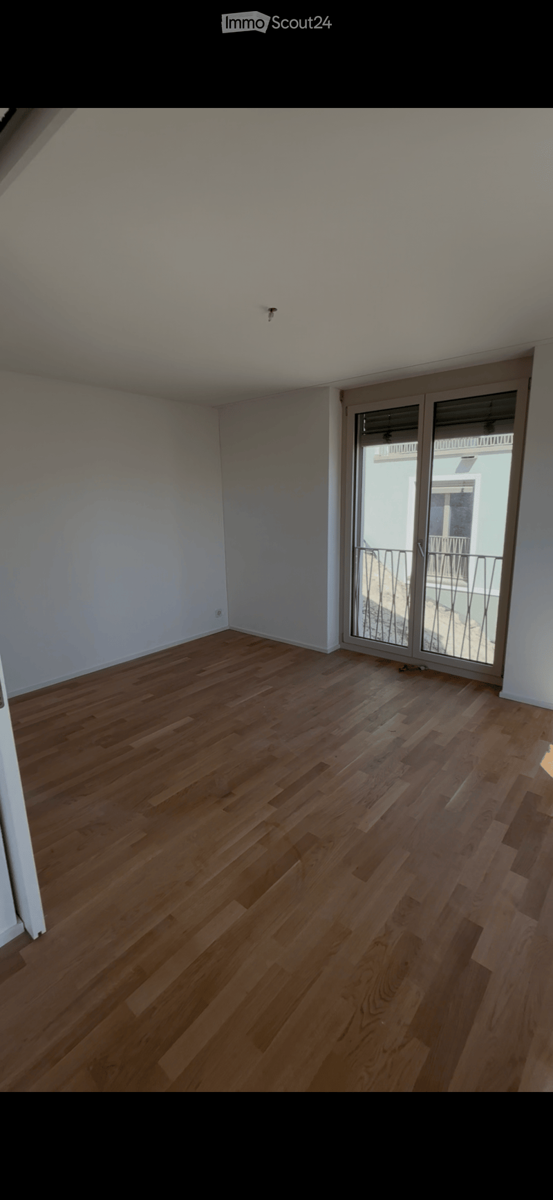 Empty room with wooden flooring and white walls, featuring a large sliding glass door leading to a balcony.