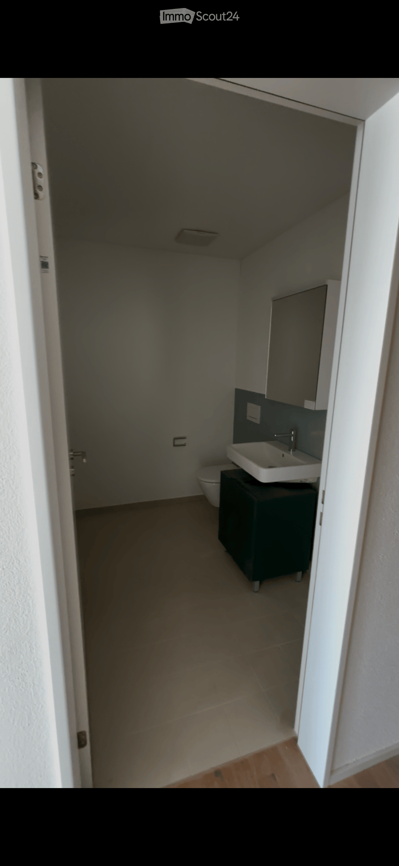 Modern bathroom with a white sink, chrome faucet, dark cabinet, and toilet. Light-colored tiled floor and white walls.