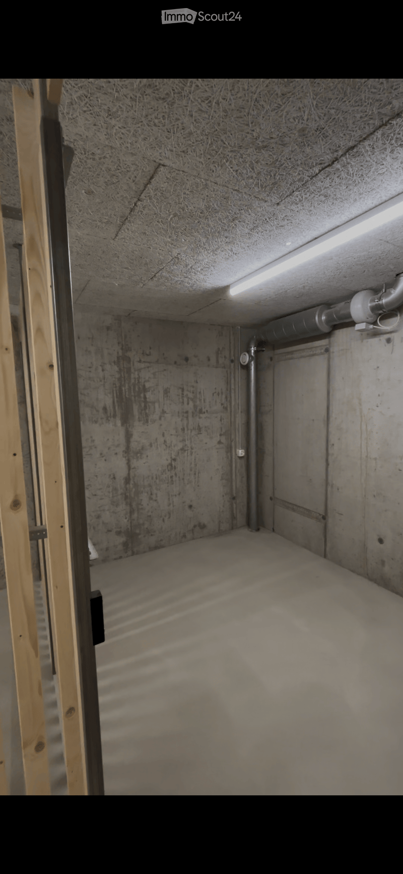 Empty unfinished basement space with concrete walls and floor, exposed wooden framing, and a small window at the top.