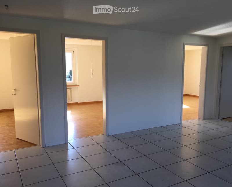 Empty room with tiled floor and wooden flooring visible through open doors, with no furniture or equipment present.