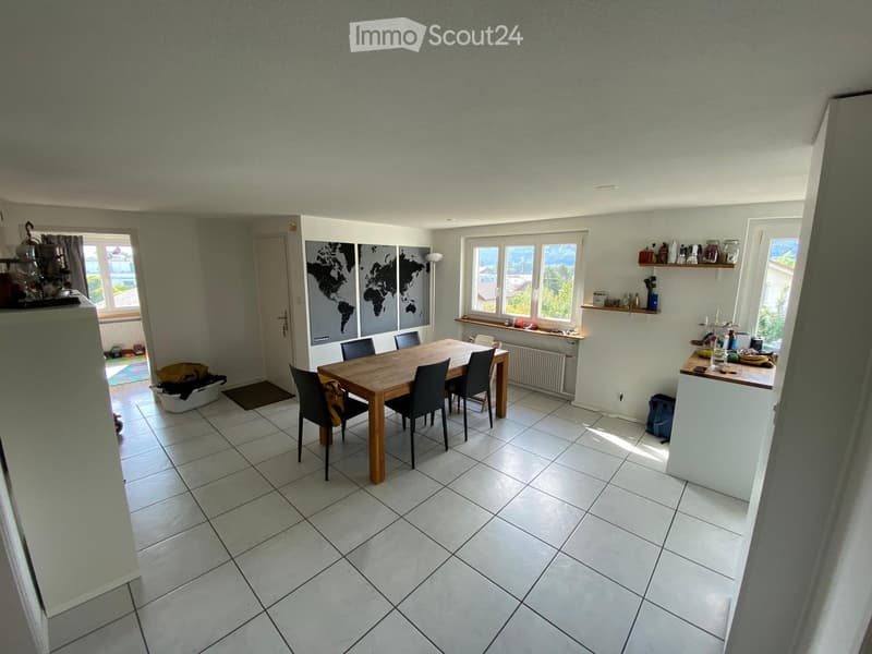 Dining area with a wooden dining table, six chairs, a kitchen counter with shelves, and a world map on the wall.