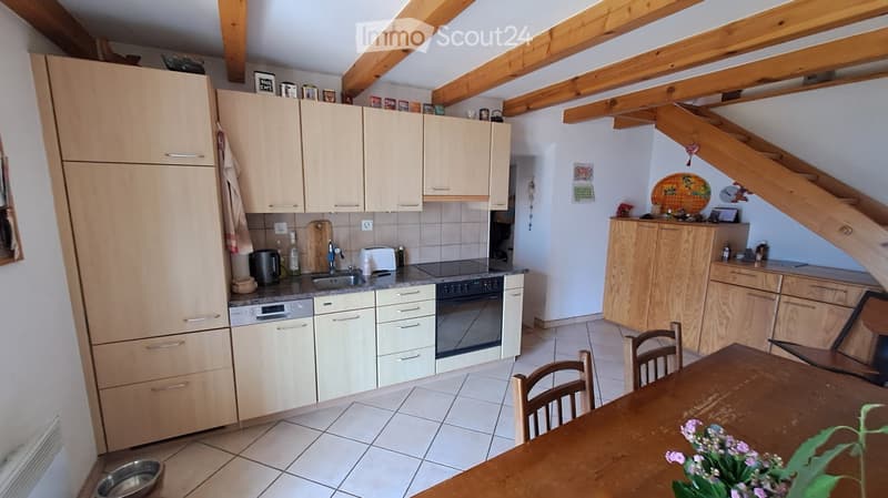 Bright kitchen with light wooden cabinets, stainless steel appliances, and a dining area with a wooden table and chairs. Exposed wooden beams on the ceiling.