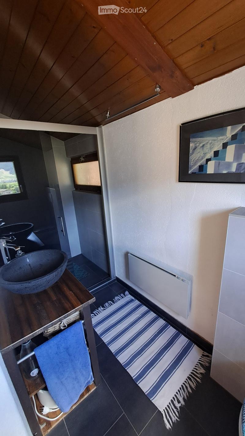 Modern bathroom with a wooden vanity, sink, mirror, radiator, and a blue and white striped rug on the floor.