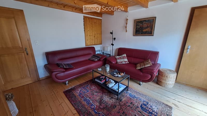 Living room with wooden floors, two red leather sofas, a coffee table, a wicker stool, and a picture frame on the wall.
