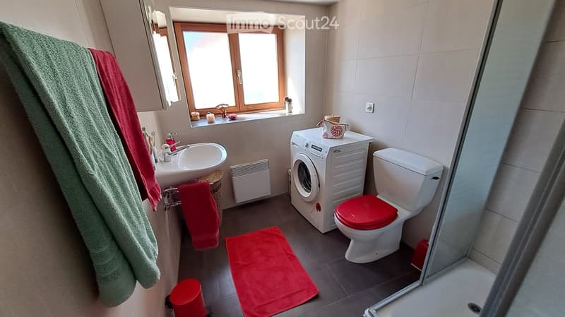 Bathroom with a sink, toilet, washing machine, and a window. Towels and a bathmat are visible.