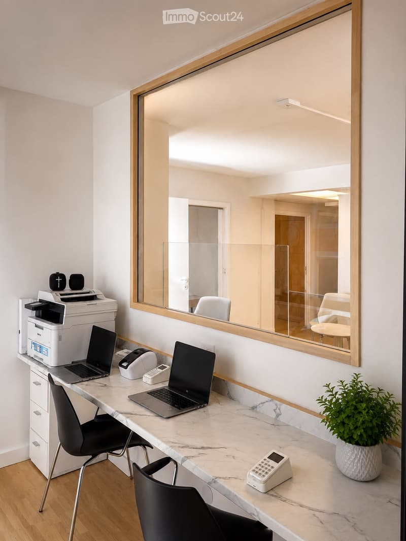 A modern office or workspace with a marble desk, two laptops, a printer, a cash register, a potted plant, and two black chairs.