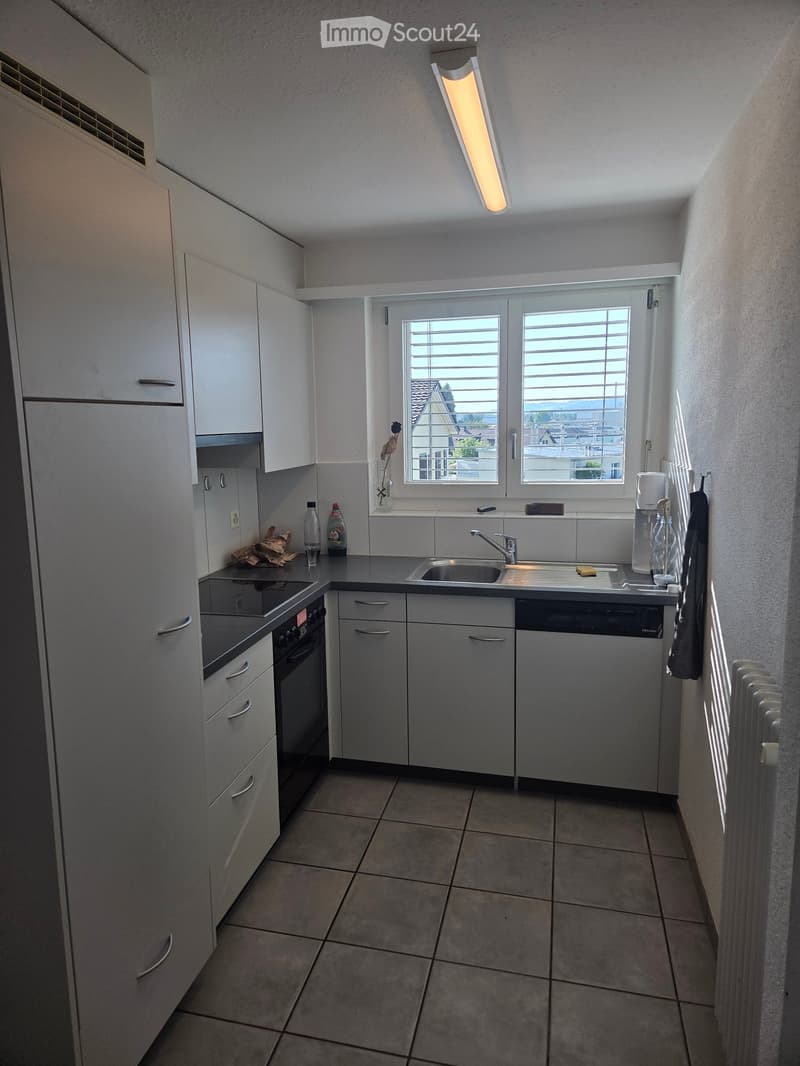 Modern kitchen with white cabinets, stainless steel appliances, tiled floor, and a window with blinds.