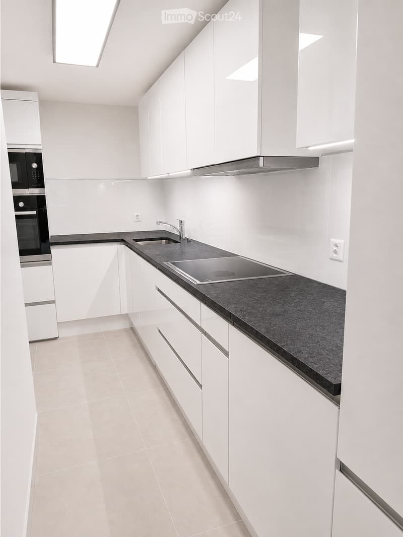 Modern kitchen with white cabinets, black countertop, built-in sink, faucet, oven, microwave, and kitchen island.