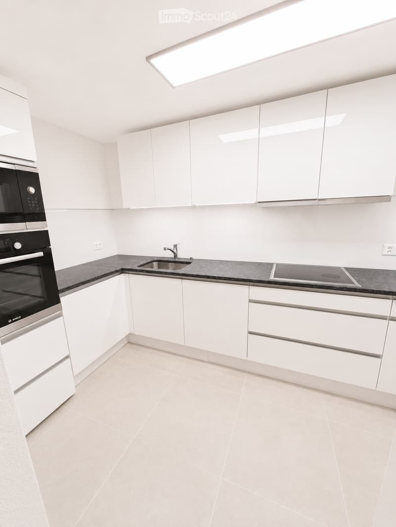 Modern kitchen with white cabinets, black countertop, built-in oven, sink, and faucet. Features a skylight above the sink.
