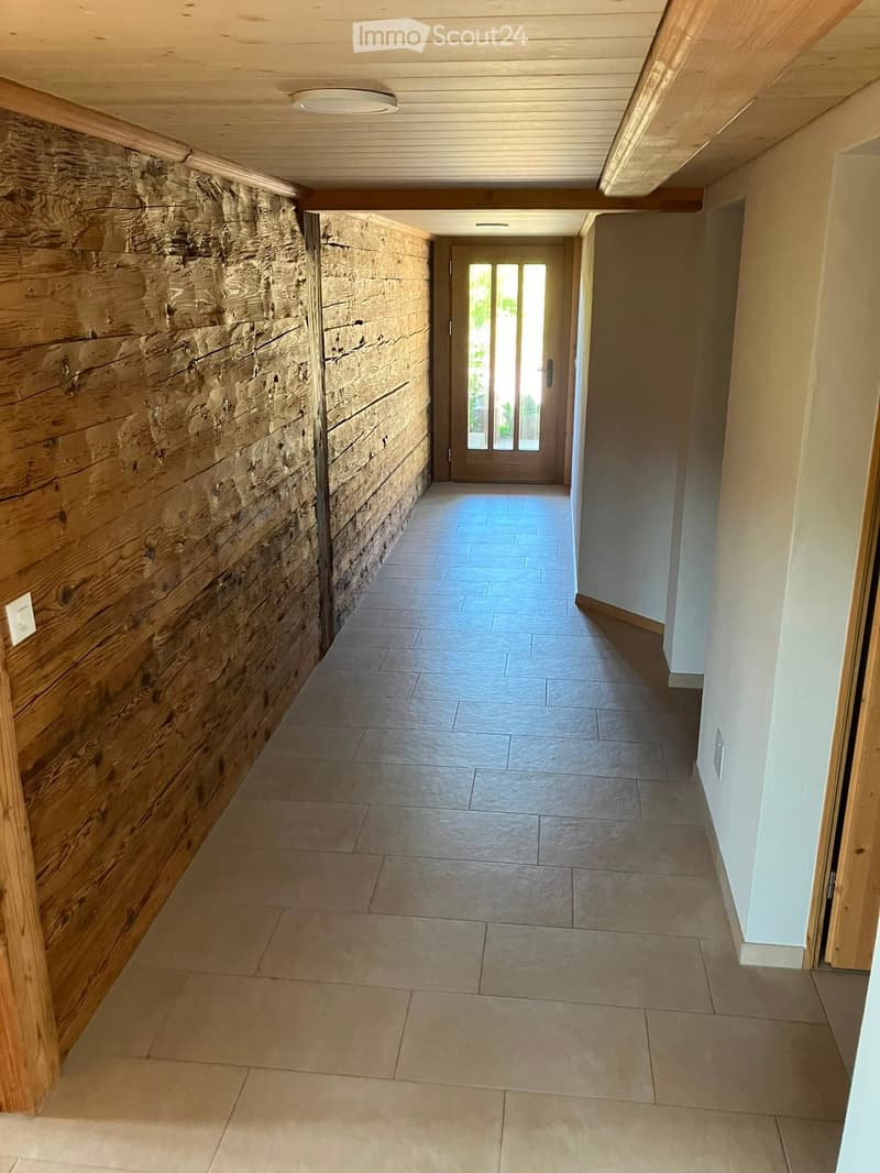 Hallway with tiled floor, wooden panel wall, and recessed lighting. Features a glass door at the end leading outside.