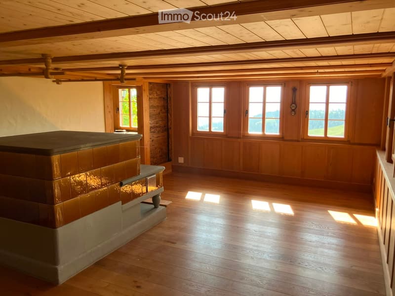 Empty room with wooden walls, wooden floor, and large windows letting in natural light. Exposed wooden beams on the ceiling.