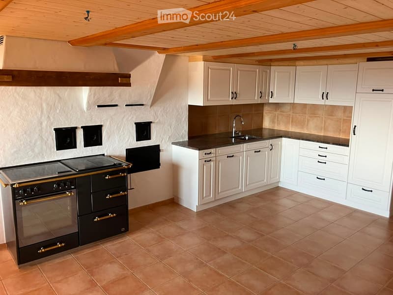 Modern kitchen with white cabinets, a black stove, and a sink, featuring a tiled floor and wooden ceiling beams.
