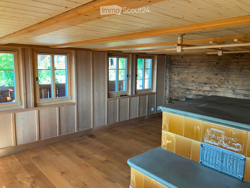 Cozy room with wooden beams, exposed wooden walls, and a fireplace with decorative tiles.