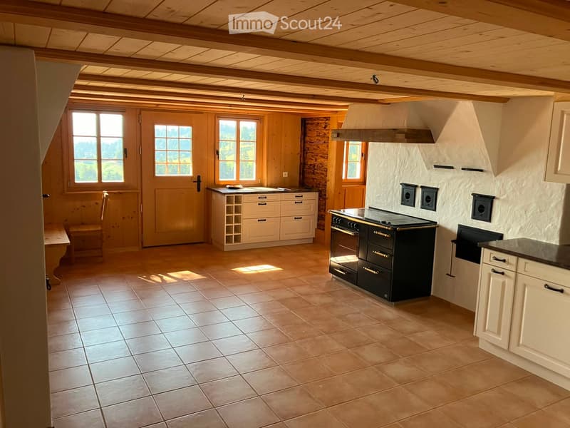 Bright, rustic kitchen with wooden beams, tiled floor, white cabinets, black stove, and a wine rack.