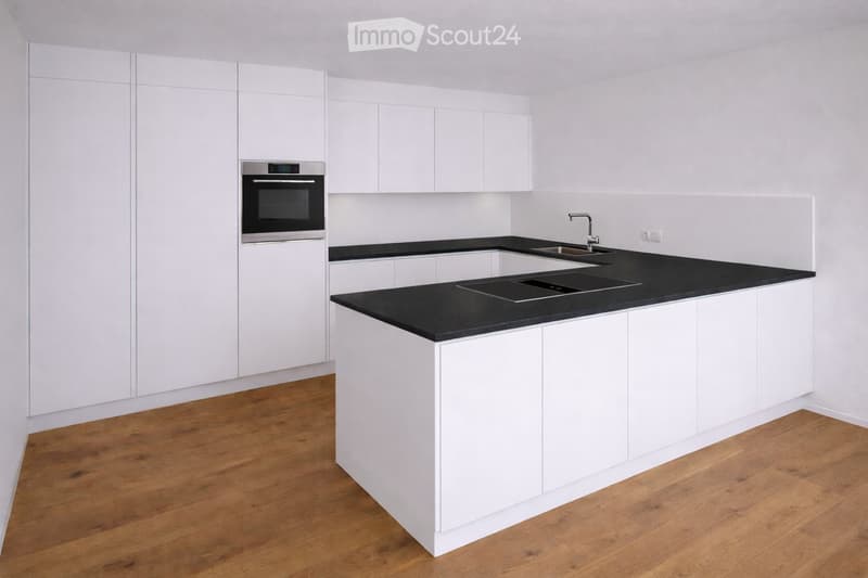 Modern kitchen with white cabinets, black countertops, and a wooden floor. Features an oven, sink, and faucet.