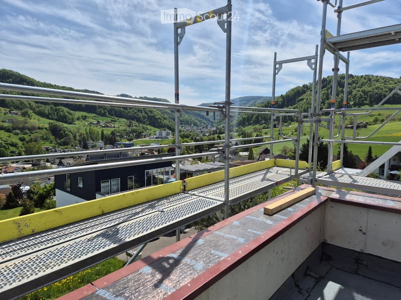 Roof terrace with metal safety railings, overlooking a green valley and scattered houses.