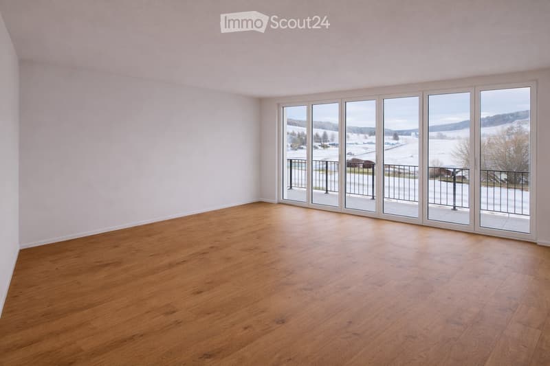 Empty room with wooden flooring and large sliding glass doors leading to a balcony with a view of a snowy landscape.
