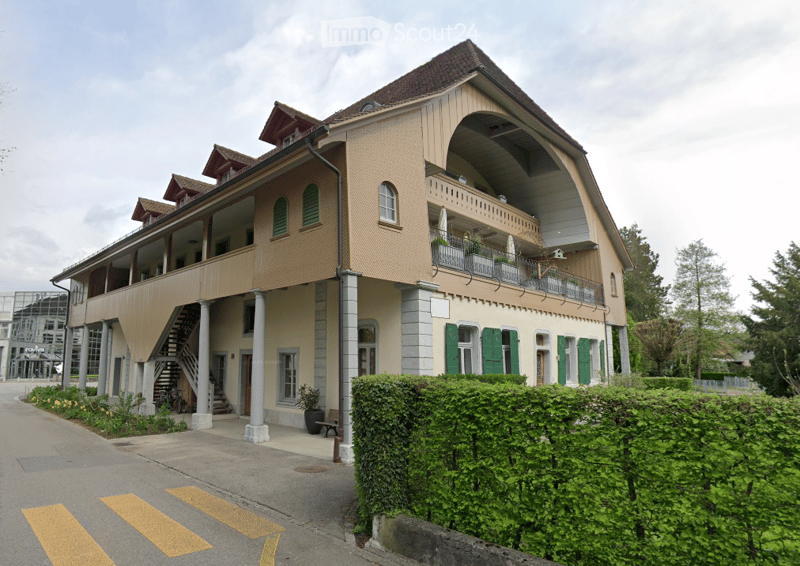 Two-story building with a balcony, green shutters, and a staircase leading to the entrance.