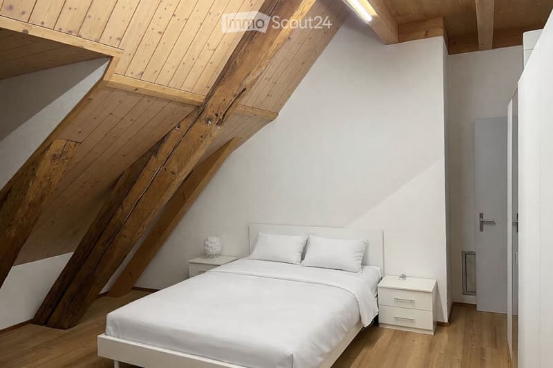 Cozy attic bedroom with wooden beams, white walls, and a double bed with white linens.
