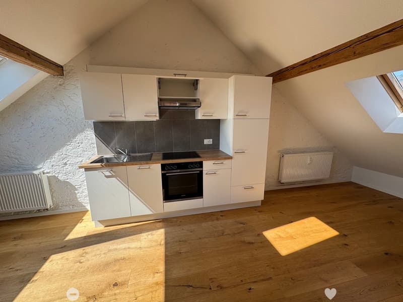 Modern kitchen with white cabinets, wooden flooring, stainless steel sink, oven, and exposed wooden beams. Natural light from skylights illuminates the space.