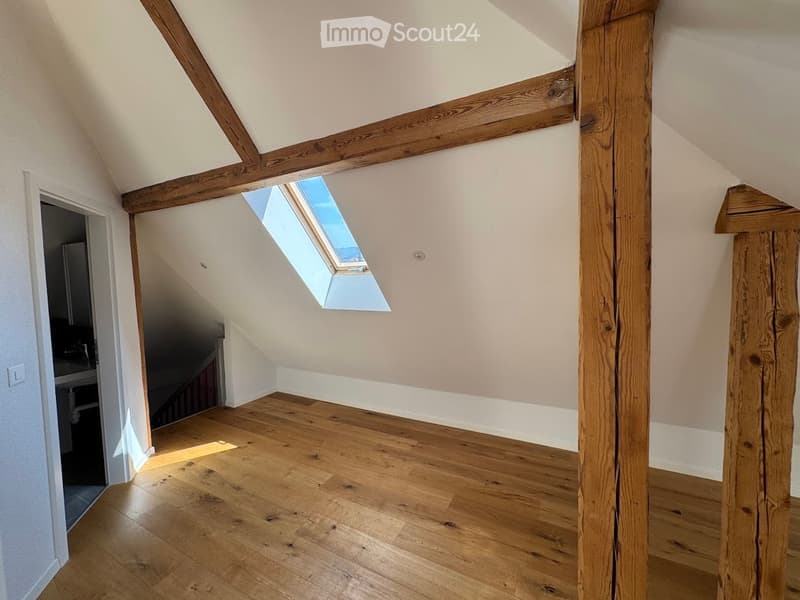 Empty attic space with wooden beams, wooden flooring, and a skylight window allowing natural light.