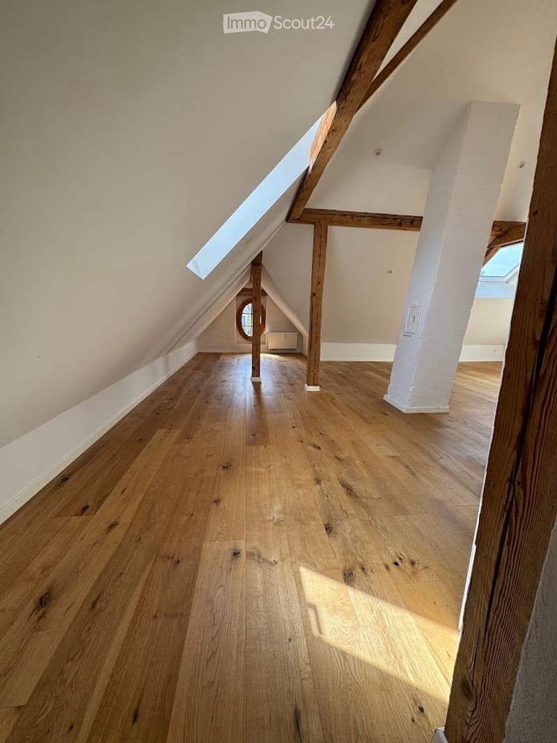 Empty attic space with wooden flooring, exposed wooden beams, and skylight windows allowing natural light.