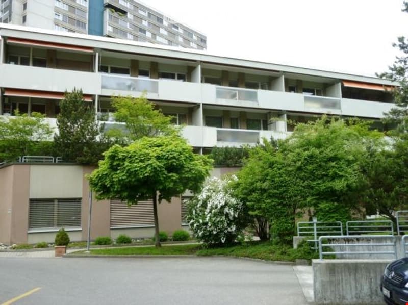 Multi-story apartment building with balconies, surrounded by greenery and trees.