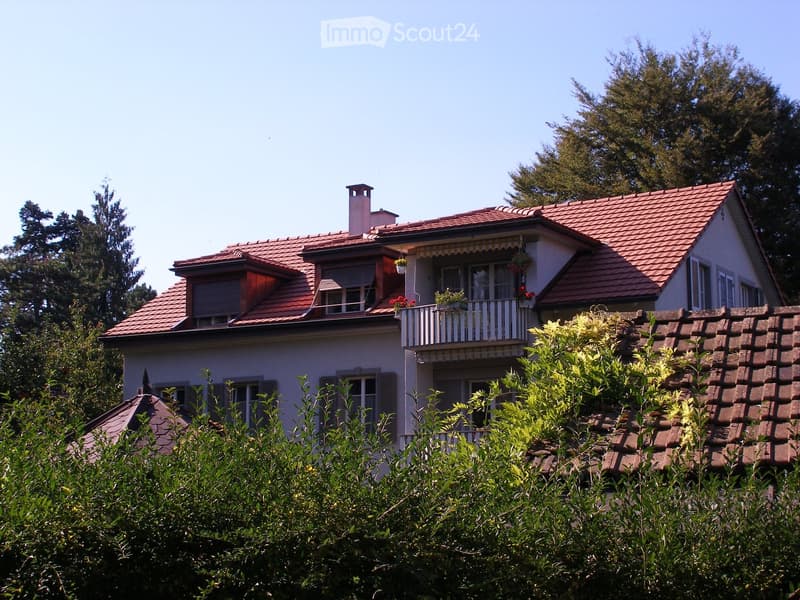 Two-story house, red roof, white walls, multiple windows, chimney, balcony with plants