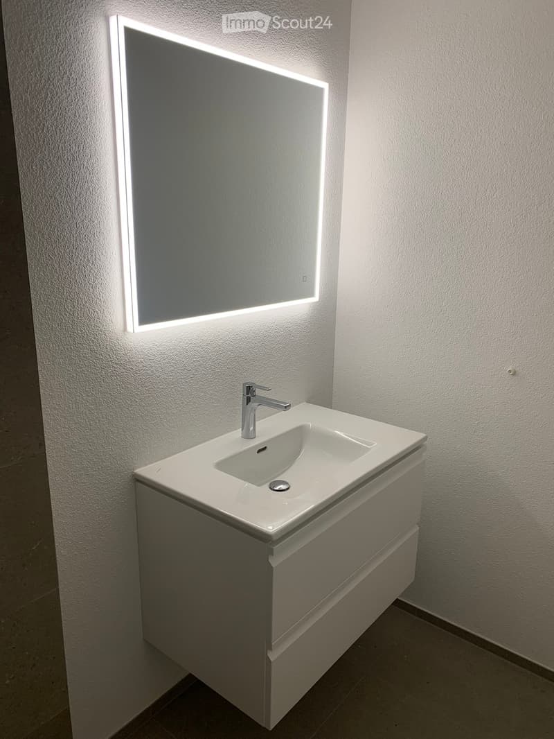 Modern bathroom with a white sink, chrome faucet, and illuminated mirror above.