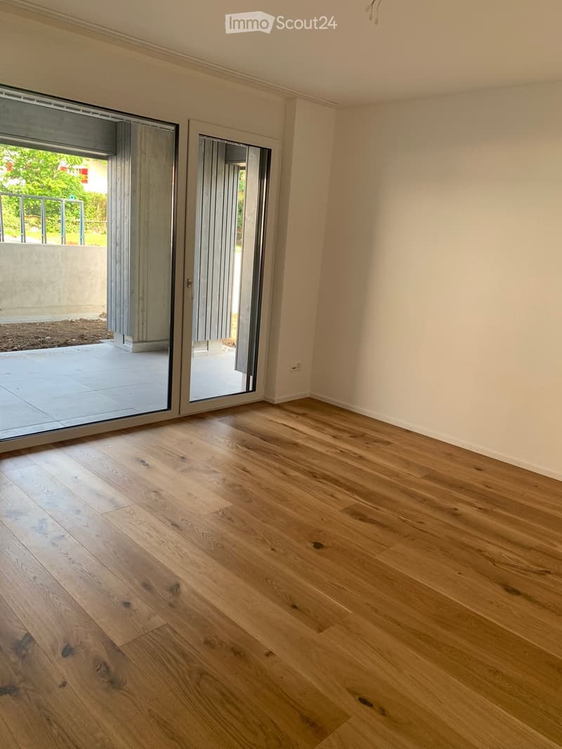 Empty room with light wooden flooring and large sliding glass doors leading to an outdoor area.